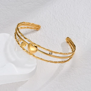 Detail of a triple-layer gold stainless steel cuff featuring a heart pendant and zircons