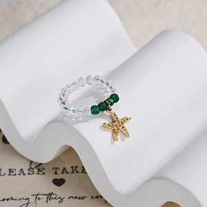Detail of beaded ring with green crystals and a gold starfish pendant on white stand