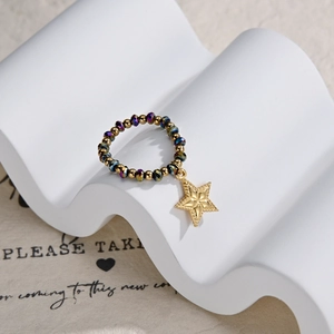 Detail of beaded ring with gold star pendant and iridescent crystals on white stand