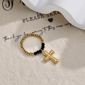 Macro detail of elastic beaded ring with black faceted beads and gold cross charm