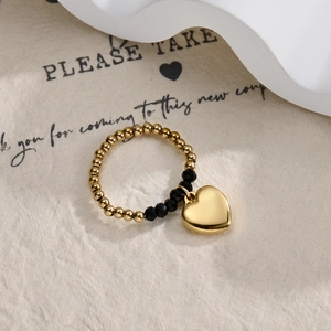 Detail of beaded ring with gold heart charm and black faceted beads on textured background