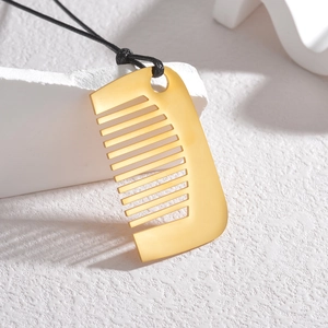 Golden comb-shaped pendant necklace with black cord shown on a minimalist white stand