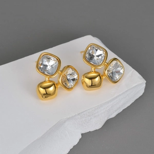 Macro shot of 18K gold plated square zircon earrings on white stone texture surface