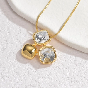 Golden square zircon pendant necklace featuring a snake chain on a white stone display