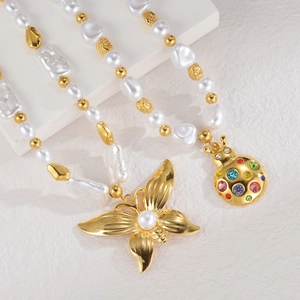Baroque pearl necklace with gold butterfly and beetle pendants on white marble stand