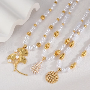 Three elegant pearl necklaces with gold leaf and teardrop pendants on white stone background
