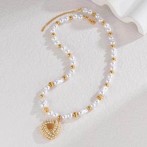 Detail of pearl necklace with gold heart pendant and baroque pearls on stone texture