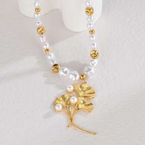Elegant gold ginkgo leaf pendant necklace with white pearls on a minimalist background