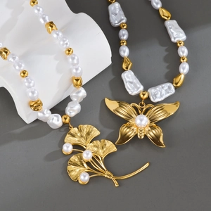 Baroque pearl necklace with gold butterfly and ginkgo leaf pendants on a stone display
