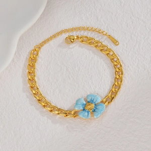 Détail du bracelet gourmette doré avec fleur en émail bleu et étiquette en acier