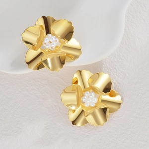 Boucles d'oreilles fleur dorées avec centres en perles sur surface blanche texturée
