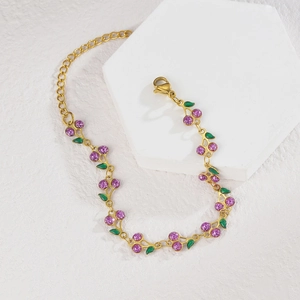 Golden cherry bracelet with purple glitter fruit and green enamel leaves on a stone stand