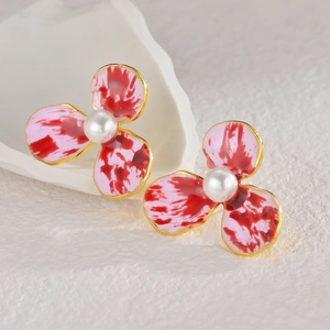 Détail des boucles d'oreilles fleur en émail rose avec une perle centrale élégante