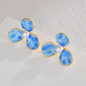 Détail de boucles d'oreilles fleurs aux pétales marbrés bleus, bord doré et perle centrale