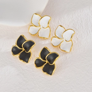 Détail de boucles d'oreilles fleurs en émail noir et blanc avec des bords dorés texturés