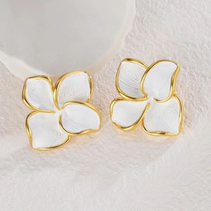 Détail des boucles d'oreilles fleurs blanches aux bords dorés sur pierre texturée