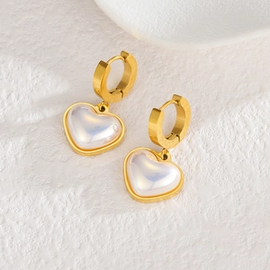 Boucles d'oreilles cœur en perle avec anneaux dorés sur un fond en pierre blanche