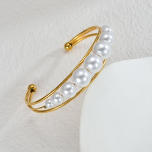 Elegant gold double-layered open cuff bracelet with pearls on a textured white surface