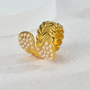 Elegant gold chevron ring with leaf accents and white pearls on a grey stone texture