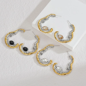 Detailed close-up of C-shaped mixed-metal earrings with textured lava finish and gemstones