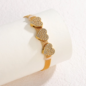 Vintage 18K gold mesh bracelet with three rhinestone heart charms on a white stand