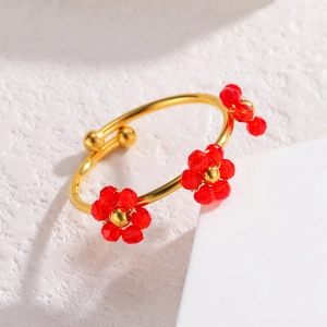 Détail d'une bague ajustable dorée avec fleurs en cristal rouge sur fond texturé blanc
