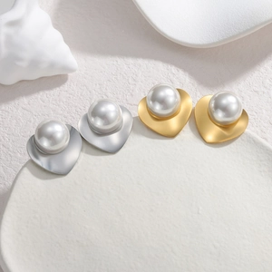 Matte gold and silver heart pearl stud earrings displayed on a white textured tray