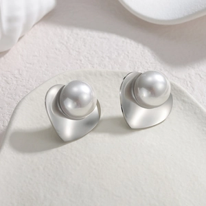 Silver minimalist heart pearl stud earrings with large white pearls on a ceramic tray