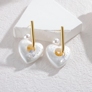 Elegant heart-shaped pearl earrings with gold accents and cubic zirconia on a stone surface