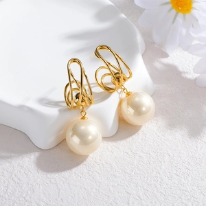 Boucles d'oreilles dorées géométriques avec perles crème sur présentoir blanc chic