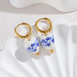 Blue and white porcelain heart earrings with gold metal hoops on a white tray
