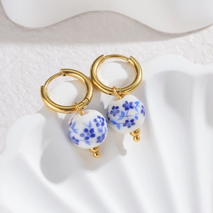 Blue floral porcelain bead earrings with gold hoops on white shell background