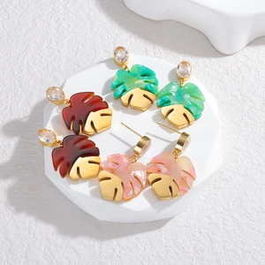 Macro shot of three pairs of tropical monstera leaf earrings with colorful resin and gold base