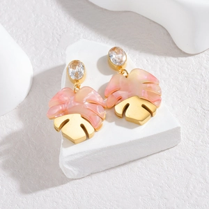 Acrylic monstera leaf earrings with rhinestones on a minimalist white stone background