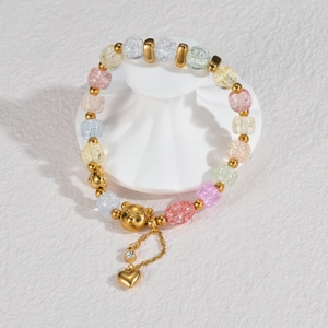 Colorful beaded bracelet with golden bear charm and heart pendant on white stone base