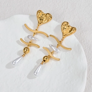 Elegant gold heart earrings with dangling pearls and metallic tassels on a white tray