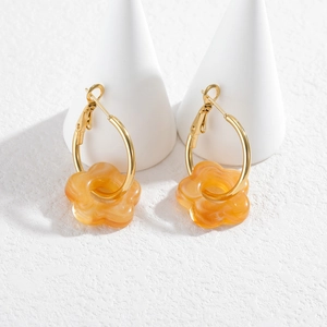 Détail de boucles d'oreilles fleurs en résine ambrée sur présentoirs blancs et anneaux dorés