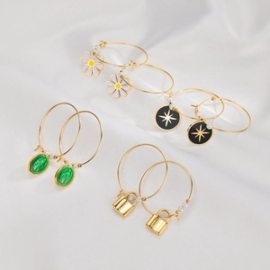 Detail of 14K gold plated hoop earrings with daisy, star, and cameo charms on white silk