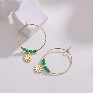 Close-up of gold hoop earrings with green beads and a daisy floral pendant on a stone block