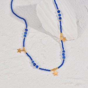 Detail einer blauen Perlenkette mit goldenen Sternanhängern auf weißem strukturiertem Stein