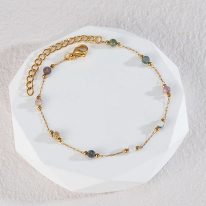 Elegant gold beaded bracelet with colorful stones displayed on an octagonal stand
