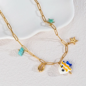 Collier doré avec pendentifs poisson, coquillage et turquoise sur un plateau en pierre