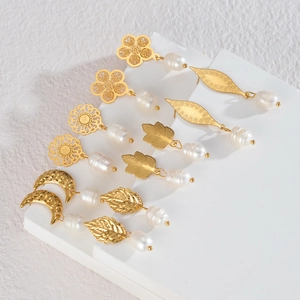 Detailed flat lay of gold titanium earrings with elegant pearls and nature-inspired charms