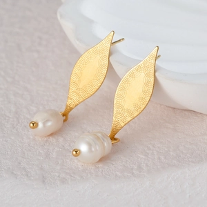 Elegant gold swirling textured earrings with baroque pearls on a minimalist white stone pedestal