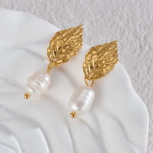 Detail of golden leaf earrings with white baroque pearl on textured ceramic tray