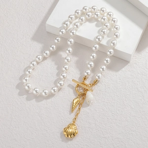 Baroque pearl necklace with gold seashell charms and T-bar clasp on white stone