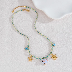 Détails macro de breloques marines en or 18K et collier en cordon tressé coloré