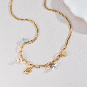 Golden stainless steel necklace with ceramic shell and turtle charms on stone background