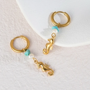 Vue macro de boucles d'oreilles hippocampe plaquées or 18K avec turquoise et perle blanche