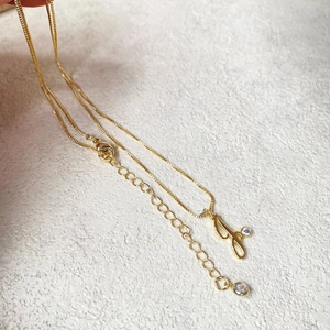 Gold plated cursive initial necklace with sparkling zircon stone on a stone background